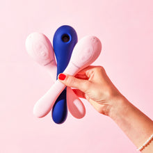 Charger l'image dans la galerie, Main tenant trois vibrateurs à succion à double stimulation Coco (deux roses et un bleu) de Puissante sur un fond rose très pâle
