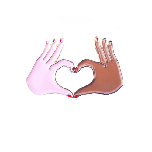 Épinglette Coucou Suzette d'une main blanche et d'une main noire avec vernis rouge  format un coeur avec les pouces et les index