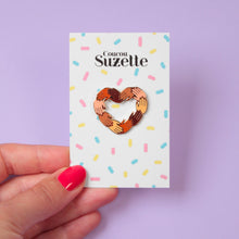 Load image into Gallery viewer, Épinglette Coucou Suzette représentant des mains de plusieurs couleurs de peau avec du vernis rouge formant un coeur sur un carton coloré sur fond mauve clair
