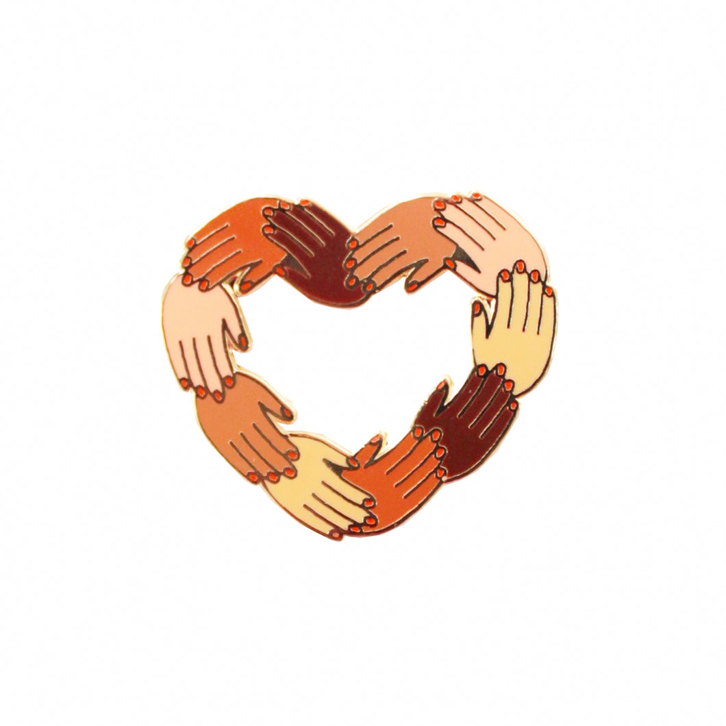Épinglette Coucou Suzette représentant des mains de plusieurs couleurs de peau avec du vernis rouge formant un coeur sur fond blanc